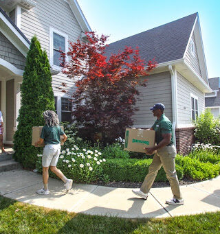 Bekins employees carrying boxes into a house.