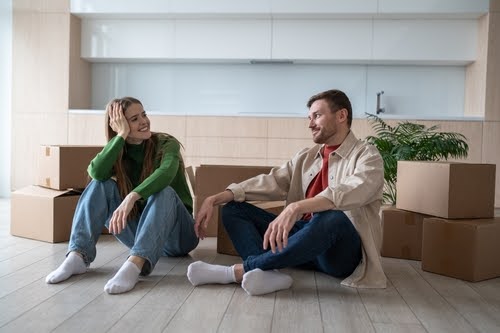 Happy family sitting on floor of new home after moving in. Smiling couple bought new apartment, investment in real estate, relocation, rental property, new beginning, mortgage loan for young family