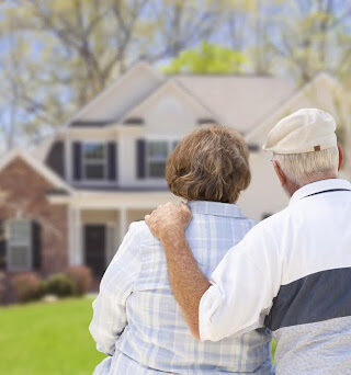 An older couple stands outside their house, looking back.