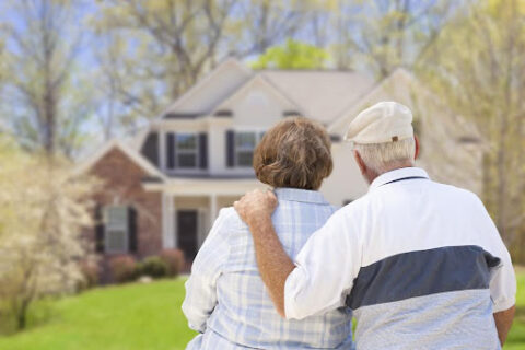 An older couple stands outside their house, looking back.