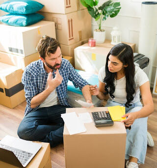 A couple calculates their expenses on top of a moving box.