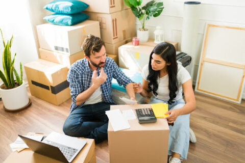 A couple calculates their expenses on top of a moving box.